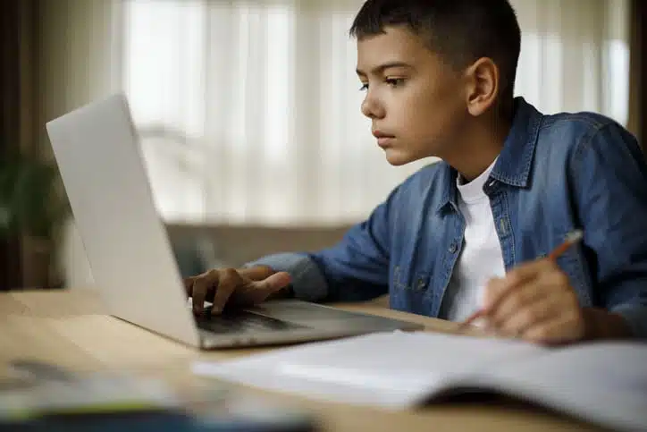 A young boy sat at a desk studying from a laptop.
