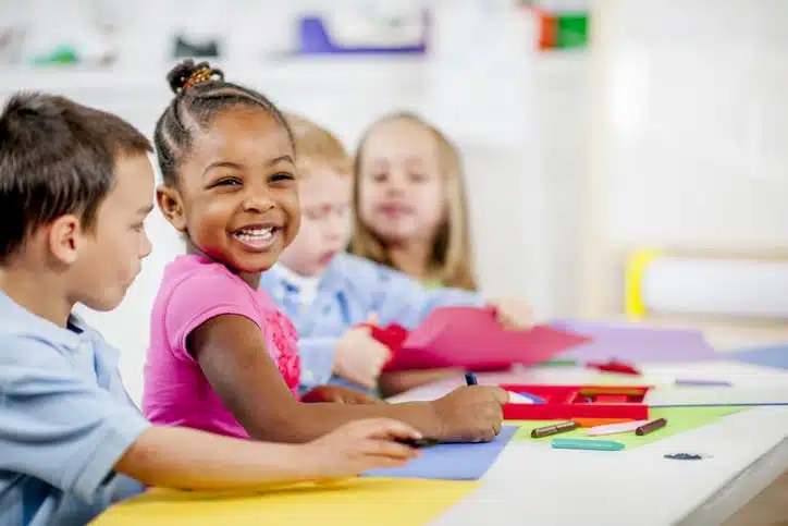 A girl drawing in a classroom and smiling